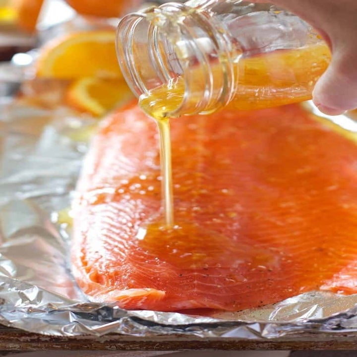 Someone pouring the honey orange glaze onto a filet of salmon.