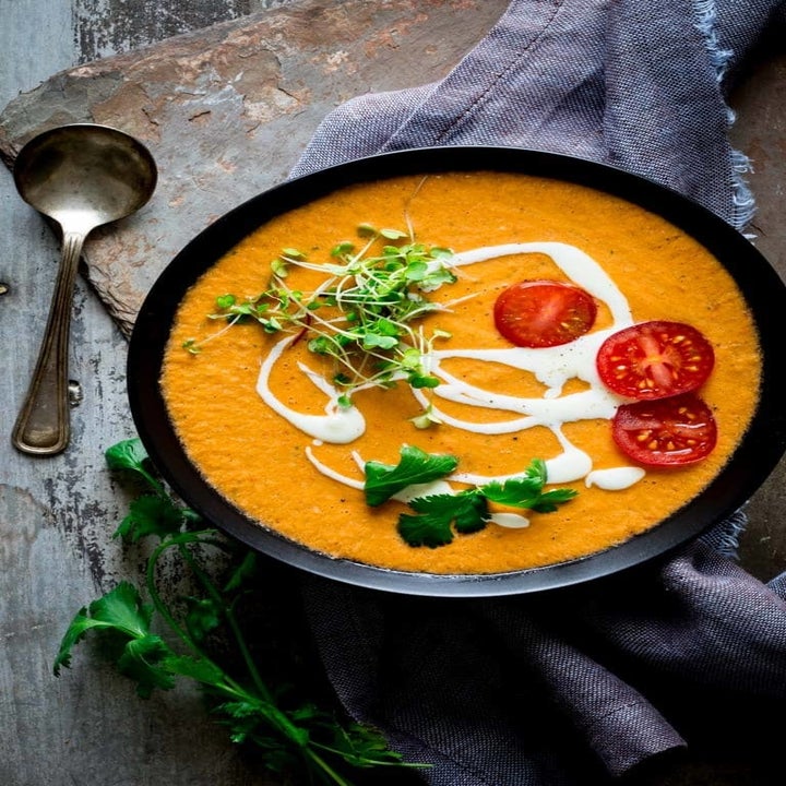 A bowl of creamy gazpacho topped with chopped cherry tomatoes, a drizzle of sour cream, and fresh herbs.