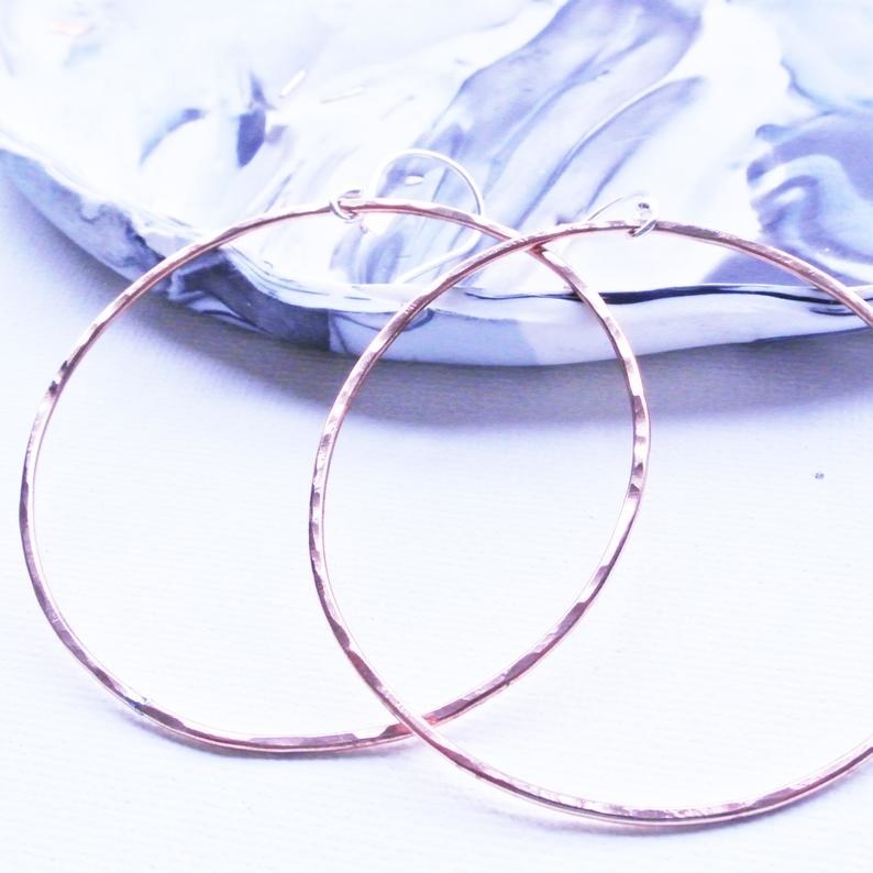 large copper tone hammered texture hoop earrings learning against a marble print jewelry dish