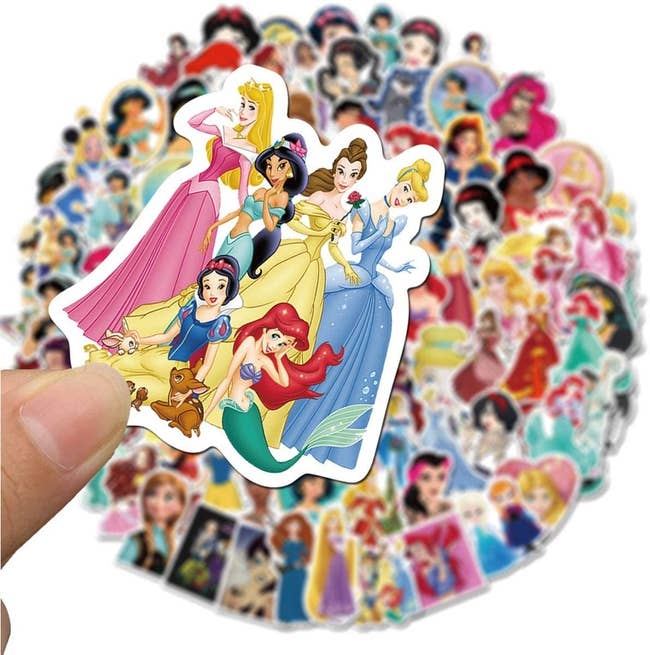 a model holding up a sticker of all the disney princesses over a pile of stickers