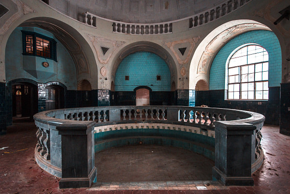 Decadent bath house that had been abandoned, bright turquoise tiles, round wall and red floor tiles