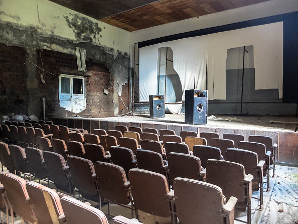 old theatre with ripped screen and decaying walls, empty seats