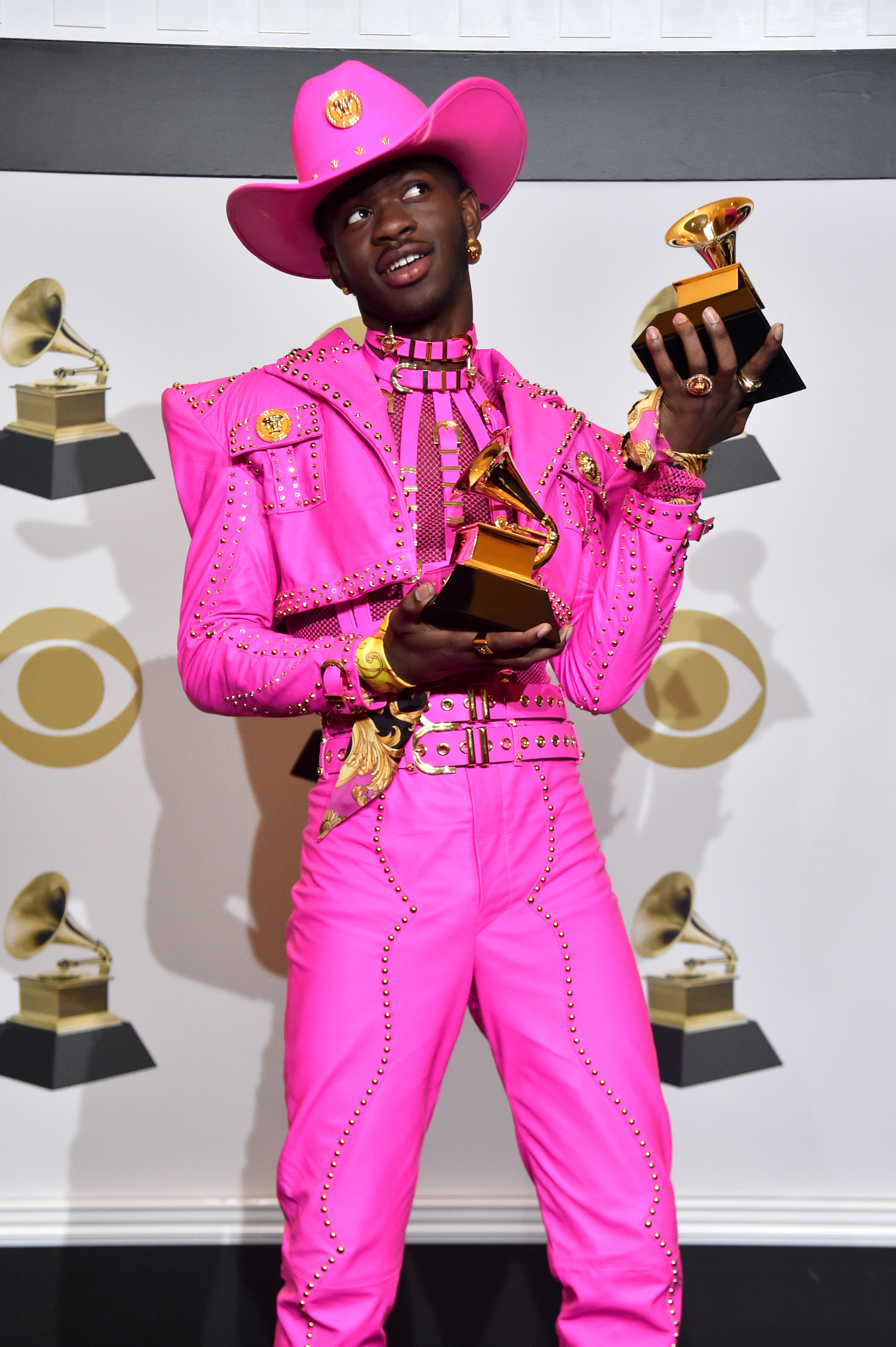 Lil Nas X holds his two Grammy awards wearing a vibrant dominatrix-type outfit and cowboy hat