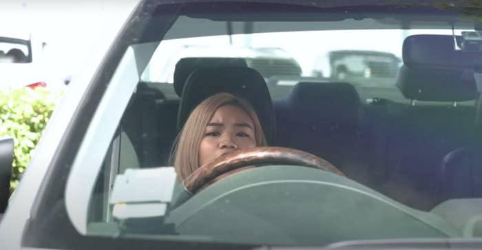A woman trying to see over steering wheel but she's too short