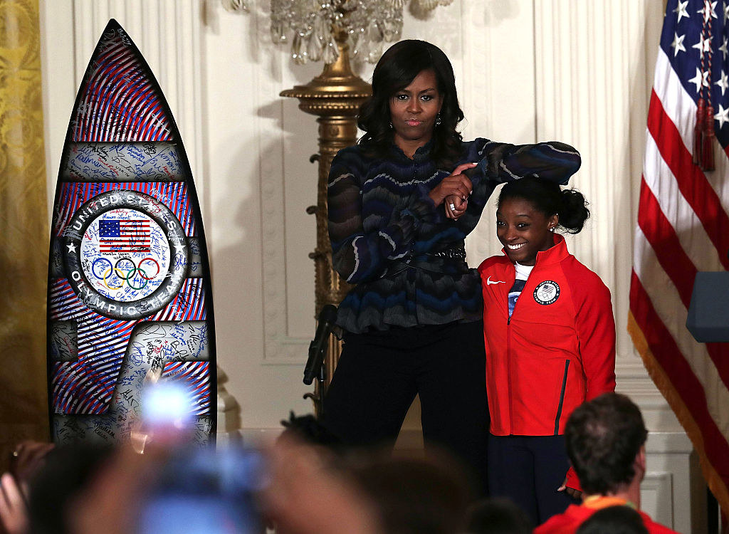 Michelle Obama resting her elbow on the head of Olympian Simone Biles