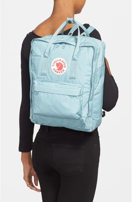 model with back facing camera carrying a light blue backpack