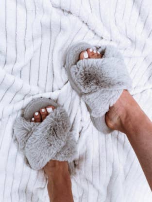 reviewer pic of feet wearing light gray faux fur slippers with open toe and plush criss-cross straps