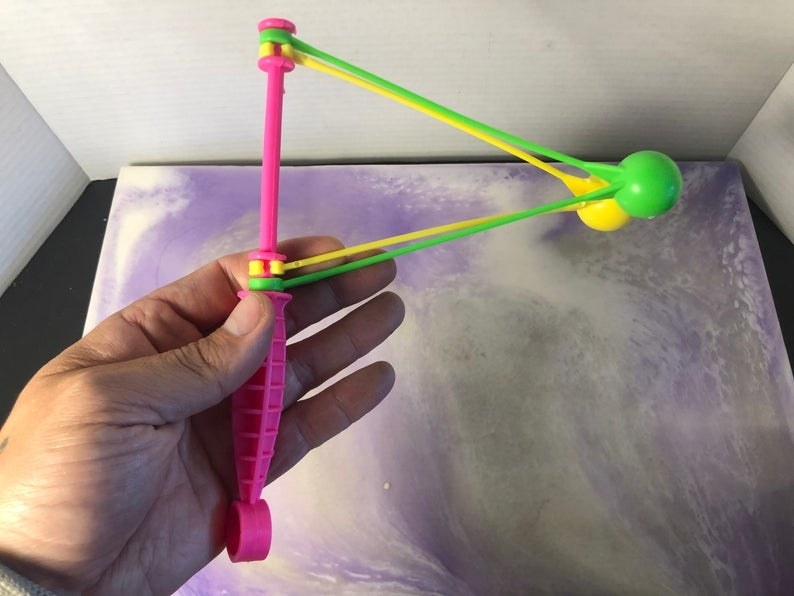 A hand holding a neon pink, yellow, and green clacker. 