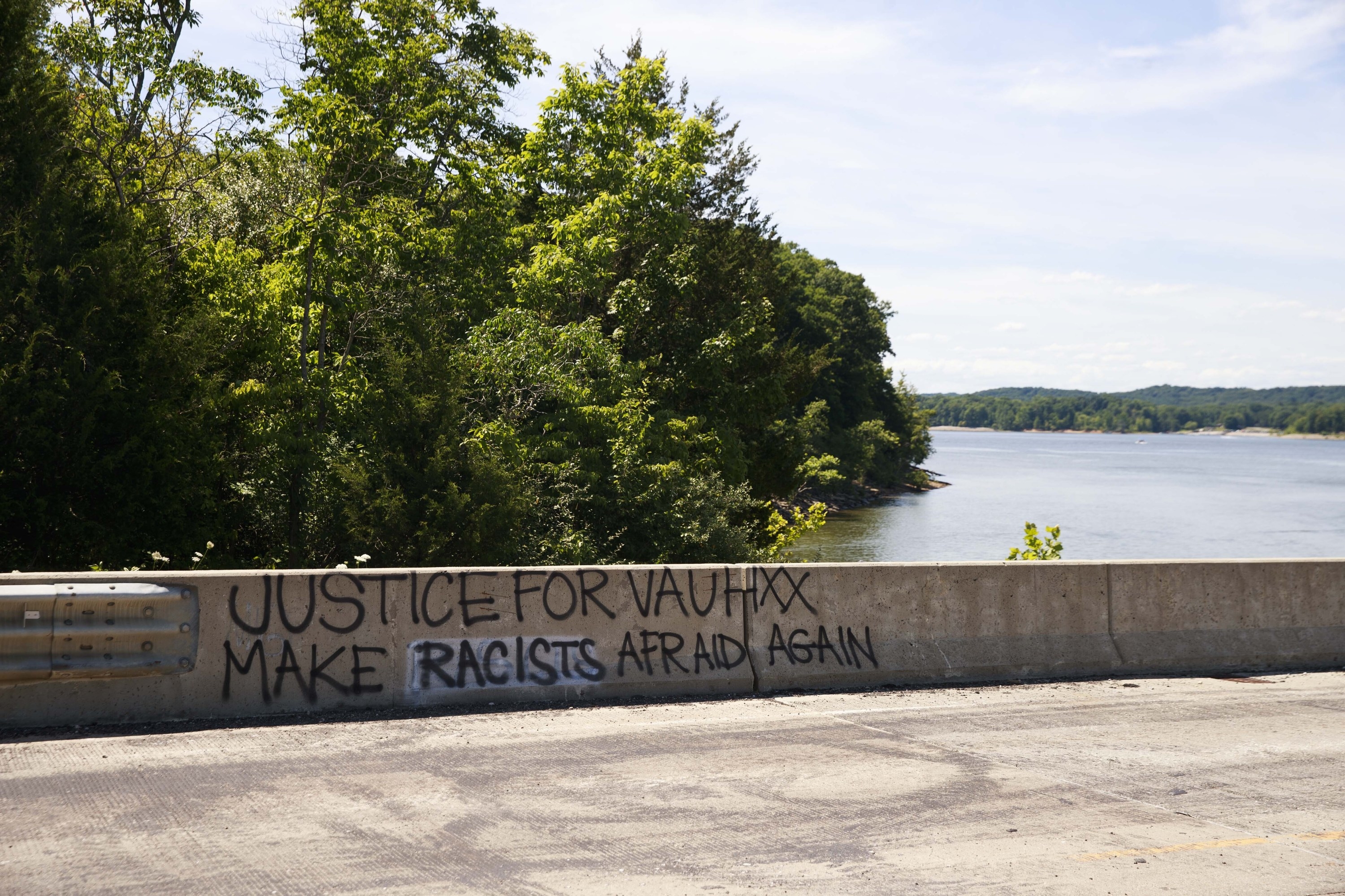 Graffiti saying &quot;Justice for Vauhxx, make racists afraid again&quot; is painted on a road barrier next to a lake with trees near where Booker was allegedly assaulted