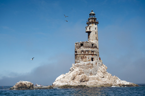 old abandoned lighthouse in the middle of the sea on a rock, birds flying around it