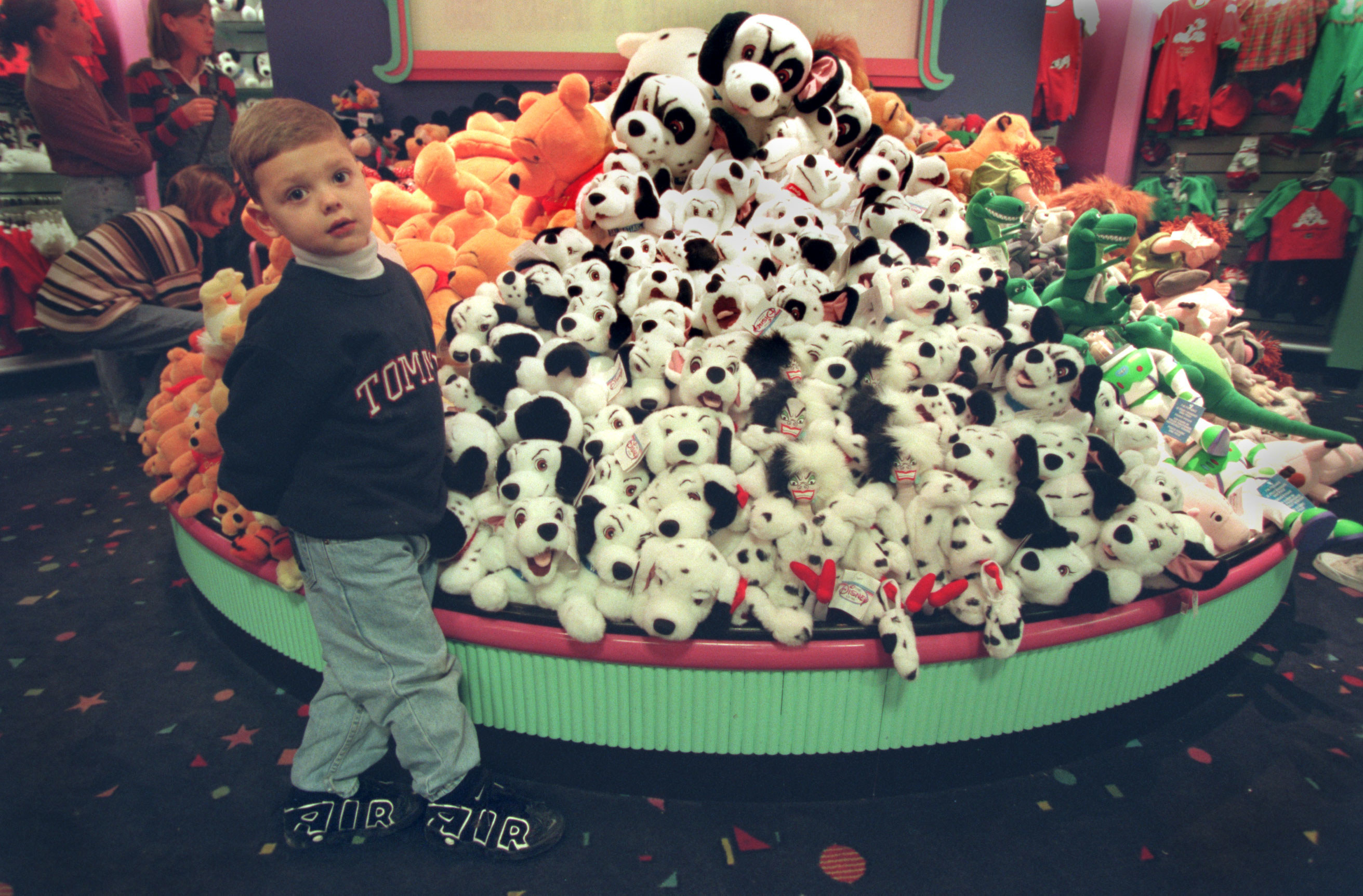 在迪士尼商店的后面，一个孩子站在一堆101只斑点狗毛绒玩具旁边。
