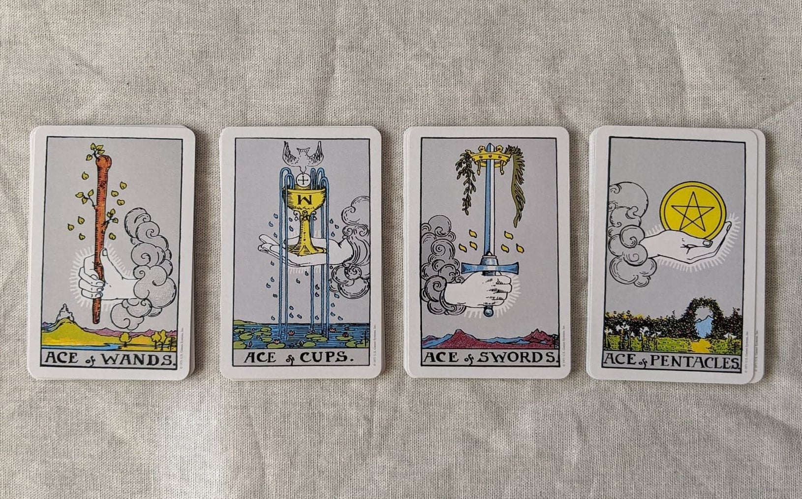 The four suits of the Rider-Waite deck lay in four decks, face up, showing the ace of wands, of cups, of swords, and of pentacles, respectively