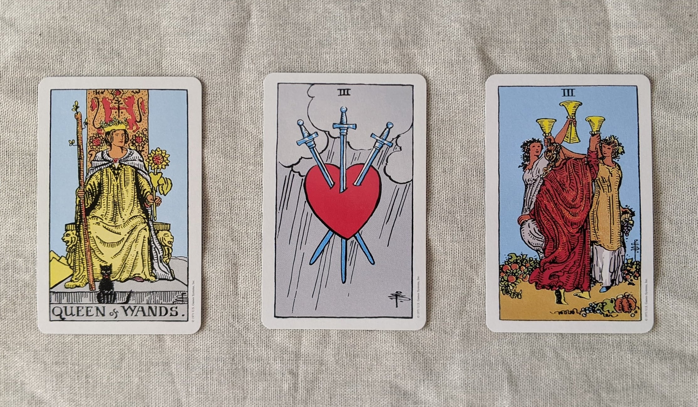 A three card spread, using the Rider-Waite deck, shows the Queen of Wands, the three of swords, and the three of cups from left to right