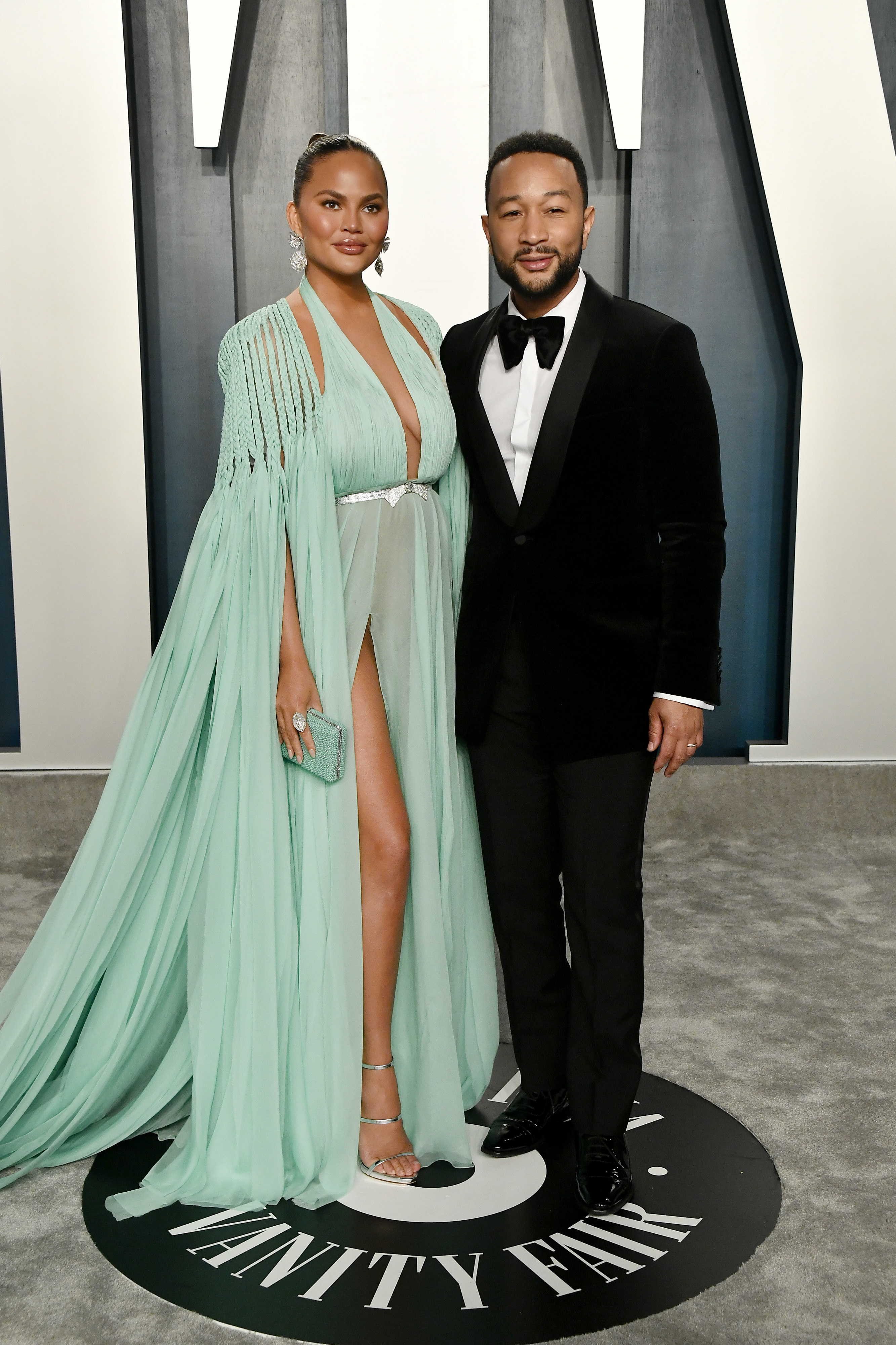 John Legend wears a black tux and Chrissy Teigen wears a teal gown at an event