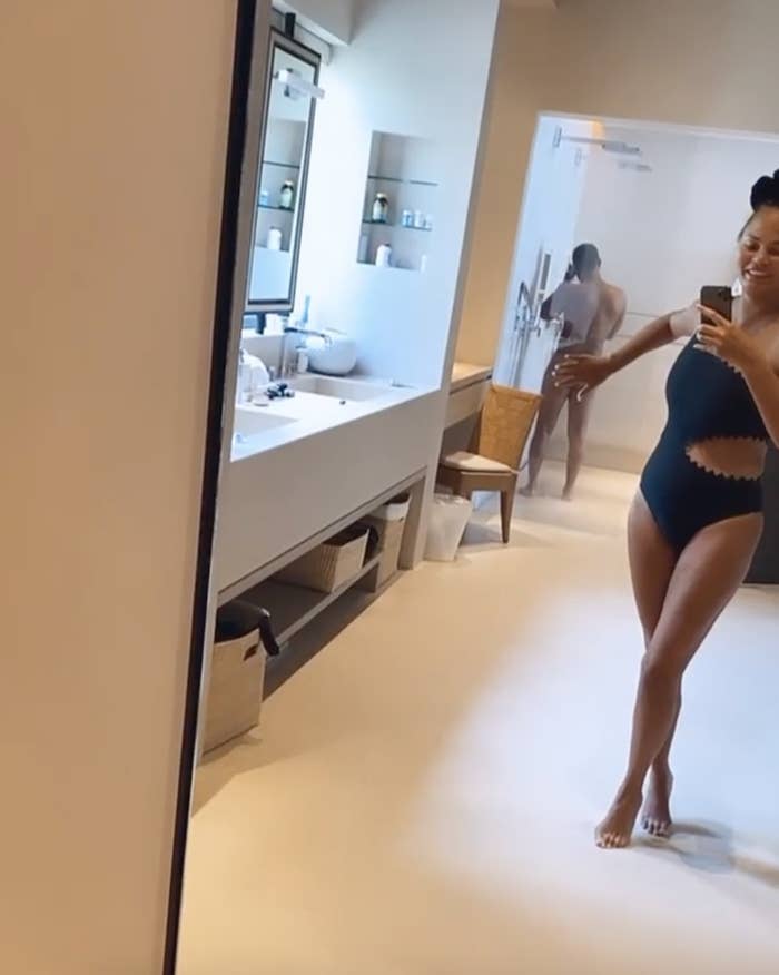 Chrissy blocks the view of John's butt with hand while wearing a bathing suit in her bathroom