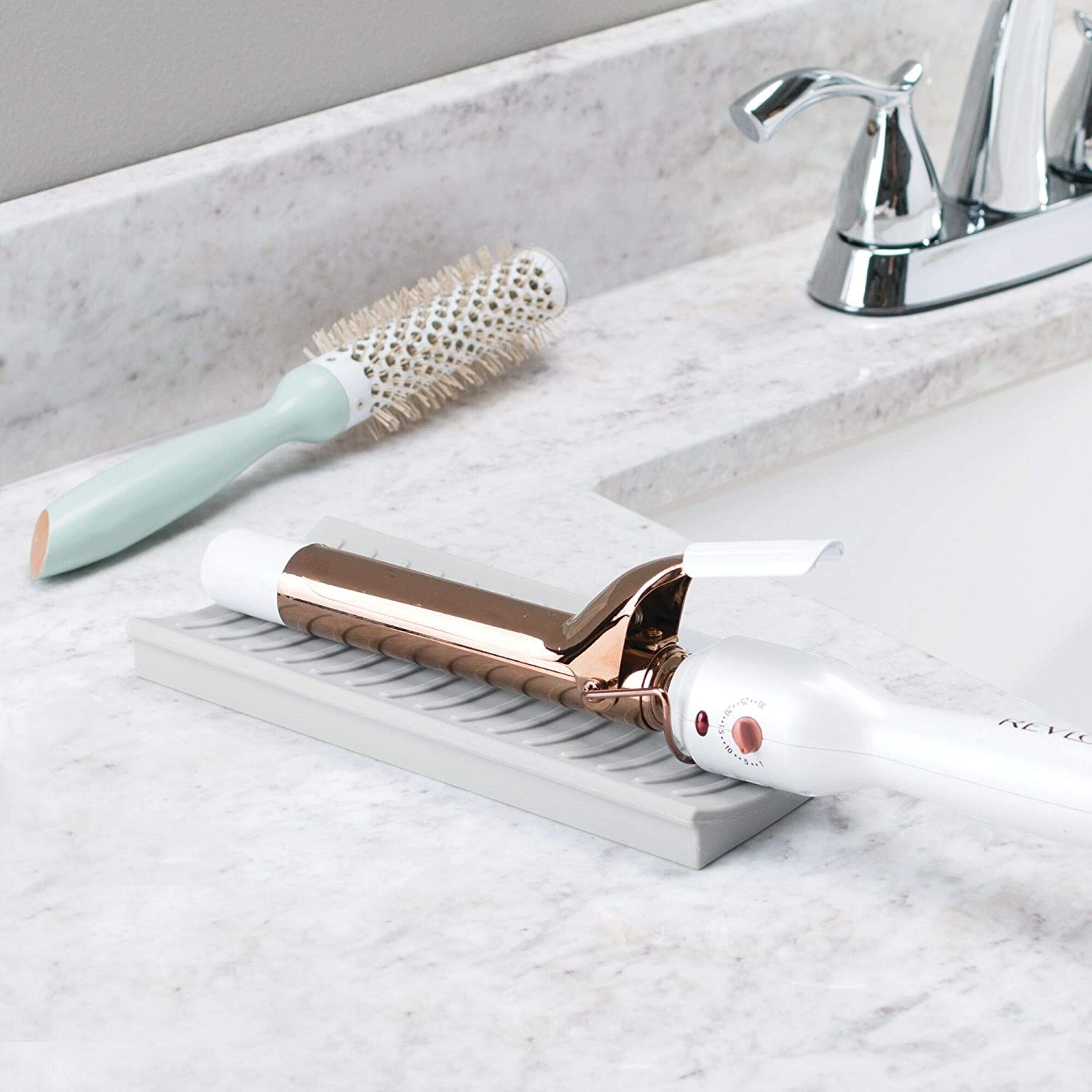 A curling iron resting on a small silicone at on a bathroom counter