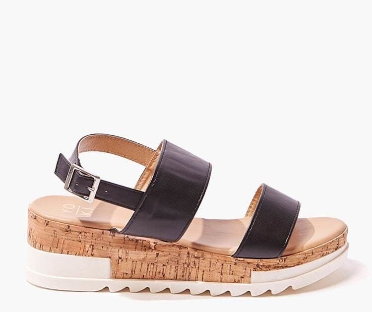 A pair of faux leather flatforms with caged front straps, shiny buckles, an open toe, and a faux cork and white grippy sole