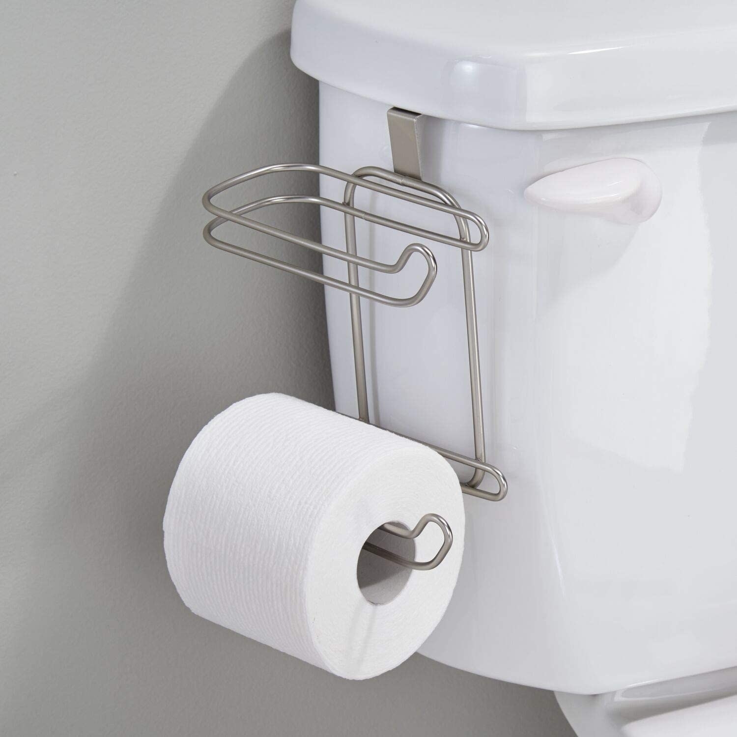 A roll of toilet paper placed on a hook that is hanging from the tank of a toilet
