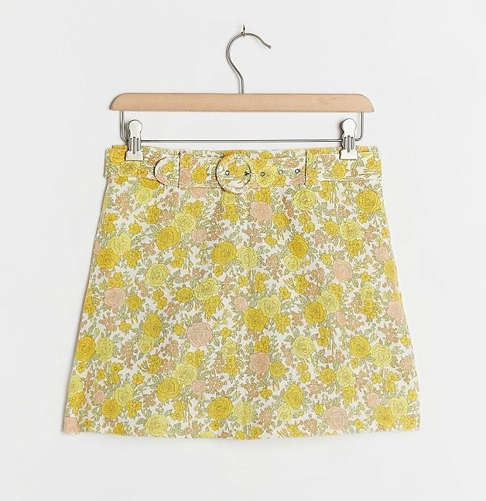 a short skort with a retro floral print of yellow and pink roses and a circular belt buckle in the same print