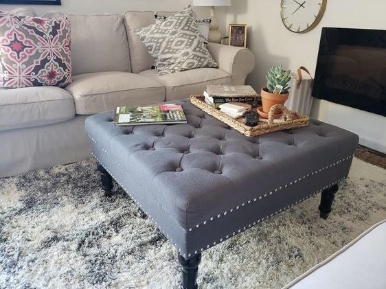 Reviewer&#x27;s photo of the tufted grey ottoman with silver studs on the side