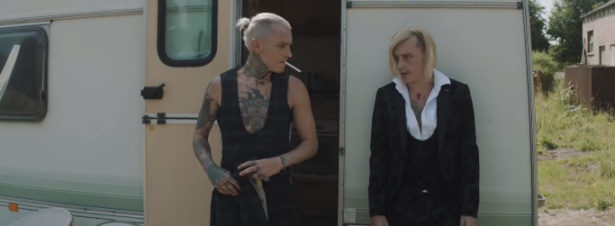 Two platinum blonde men standing in front of a caravan with the door open