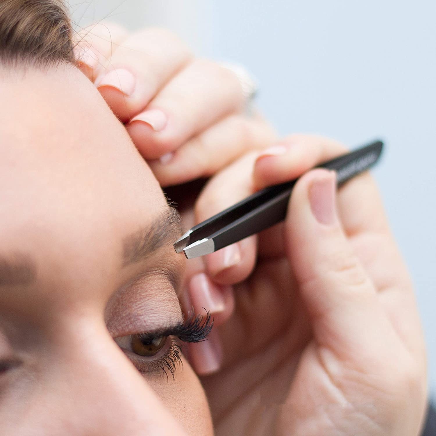 A person using the tweezers to clean up hairs around their eyebrows 