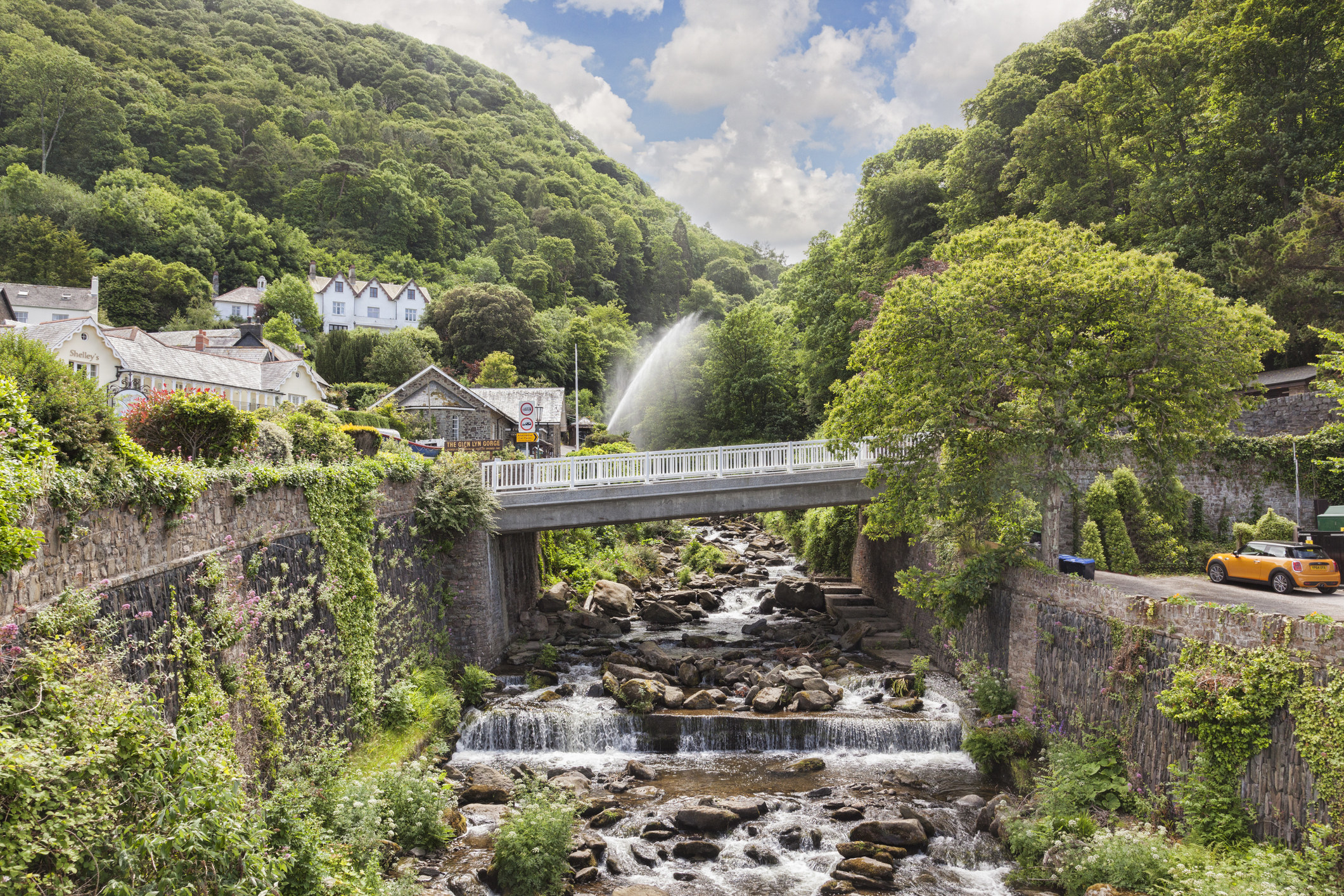 A bridge covers a river while houses sit among the greenery of the hilly scene