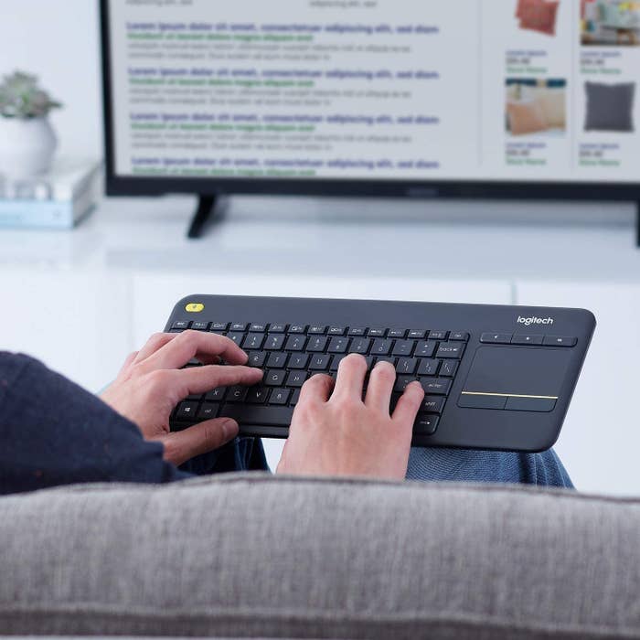 A person types on the lightweight keyboard with a large tv in the background