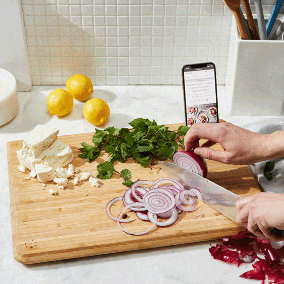 gif of someone cutting watermelon on the board and pouring the juice from a deep groove into a container, as well as cutting an onion while showing an iPhone in a special phone cutout