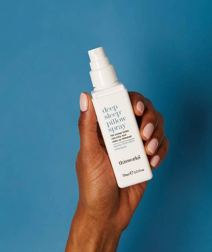 Model&#x27;s hand holding the white spray bottle with the words &quot;deep sleep pillow spray&quot; written on it in blue