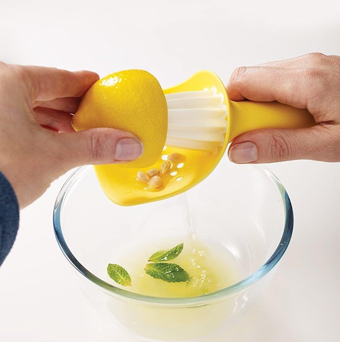 A person juices a lemon over a bowl where a few seeds are caught in the colander attachment