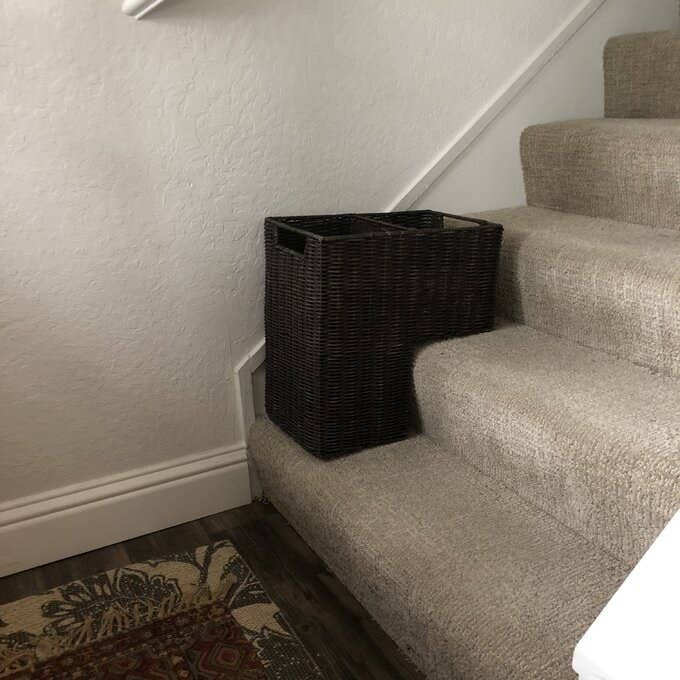 The wicker basket is sitting on a carpeted staircase. It&#x27;s shaped like a square with a corner cut out. That cutout corner is what sits on the steps.