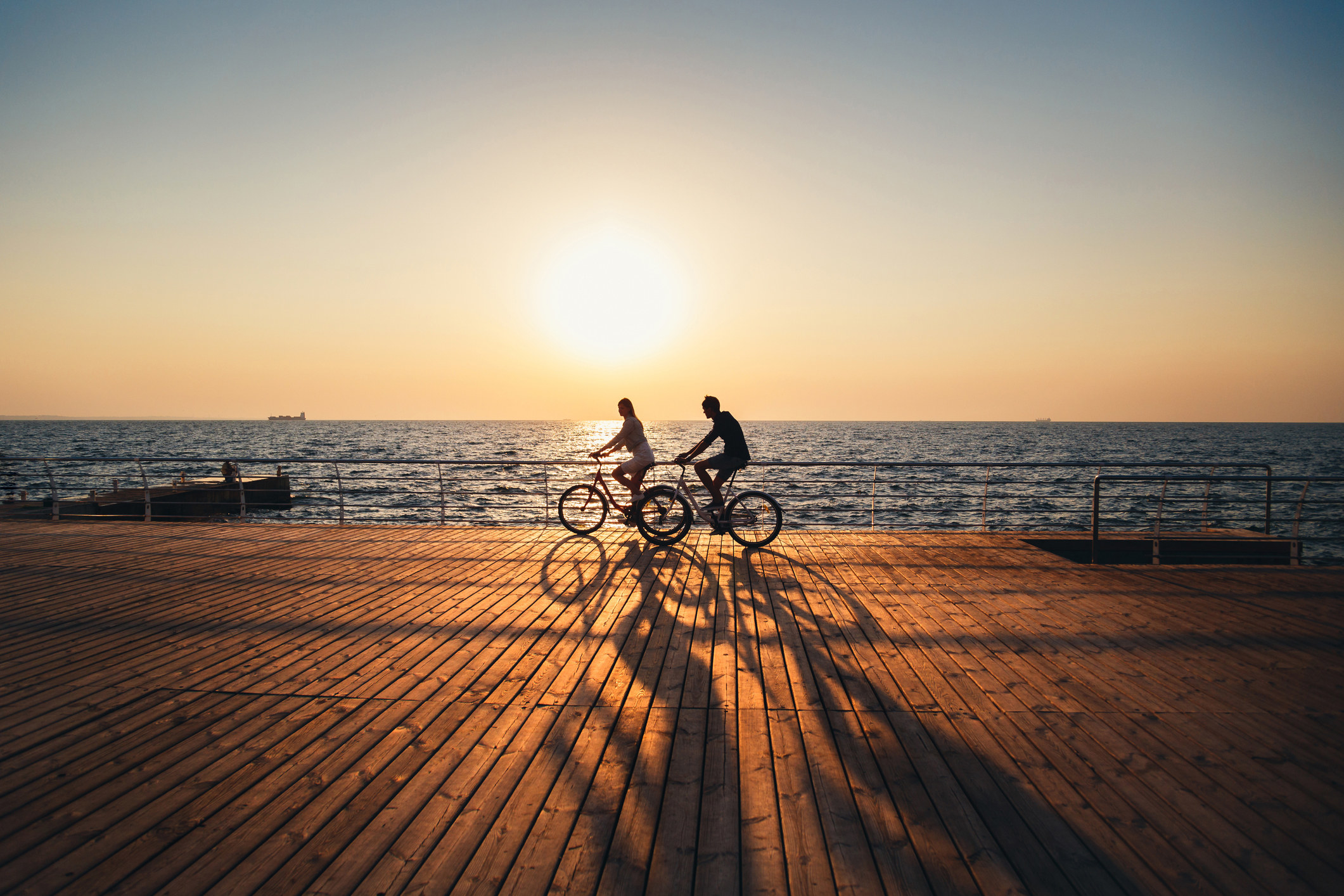 Two people riding their bikes on a boardwalk.