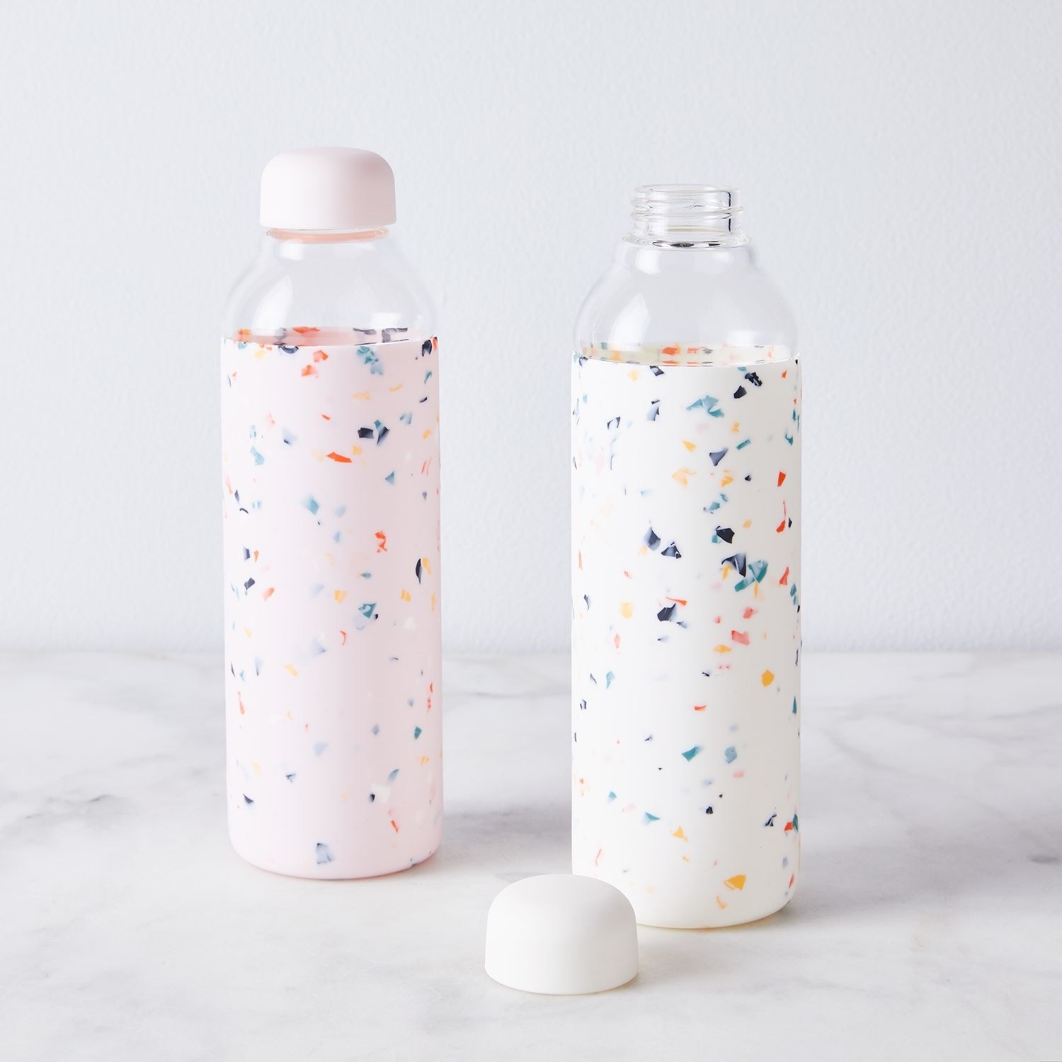 A pair of water bottles with speckled primary colors and rounded caps 