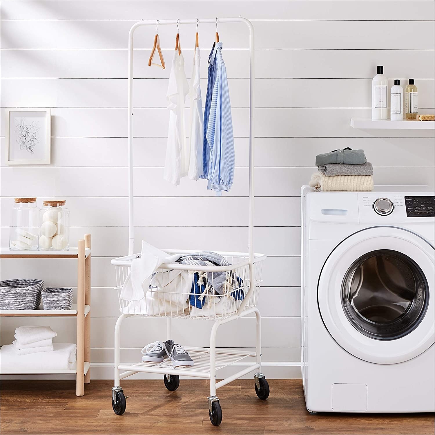 A small square laundry basket with wheels It has a tall hanging rack above it 