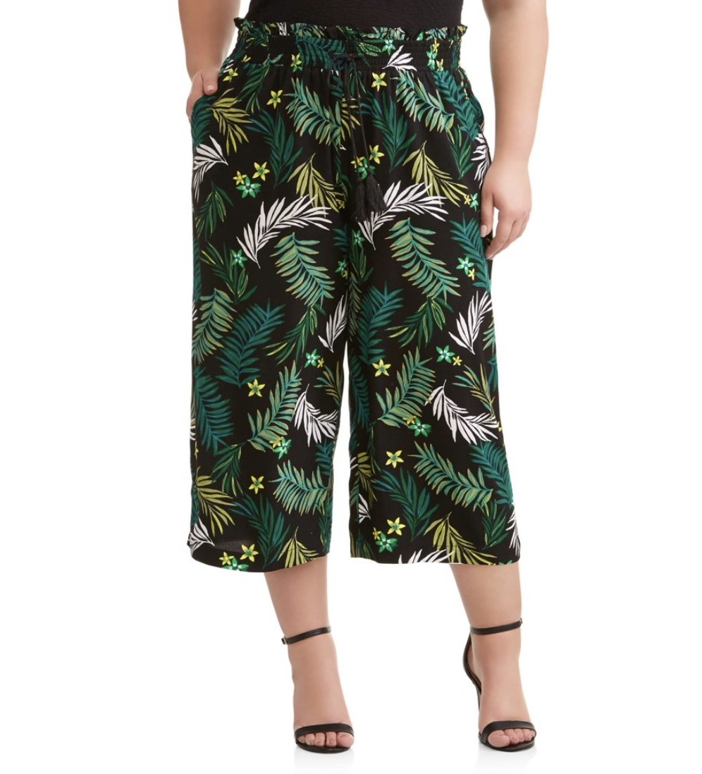 A model in a black cropped wide-length pant with palm leaves on it 