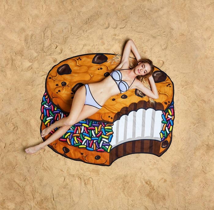 A model lying on the large towel, which looks like a chocolate chip cookie ice cream sandwich with rainbow sprinkles and a bite taken out of it