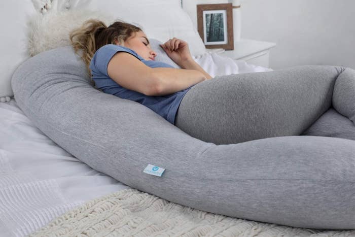 A person sleeping on their side with a long U-shaped pillow around them