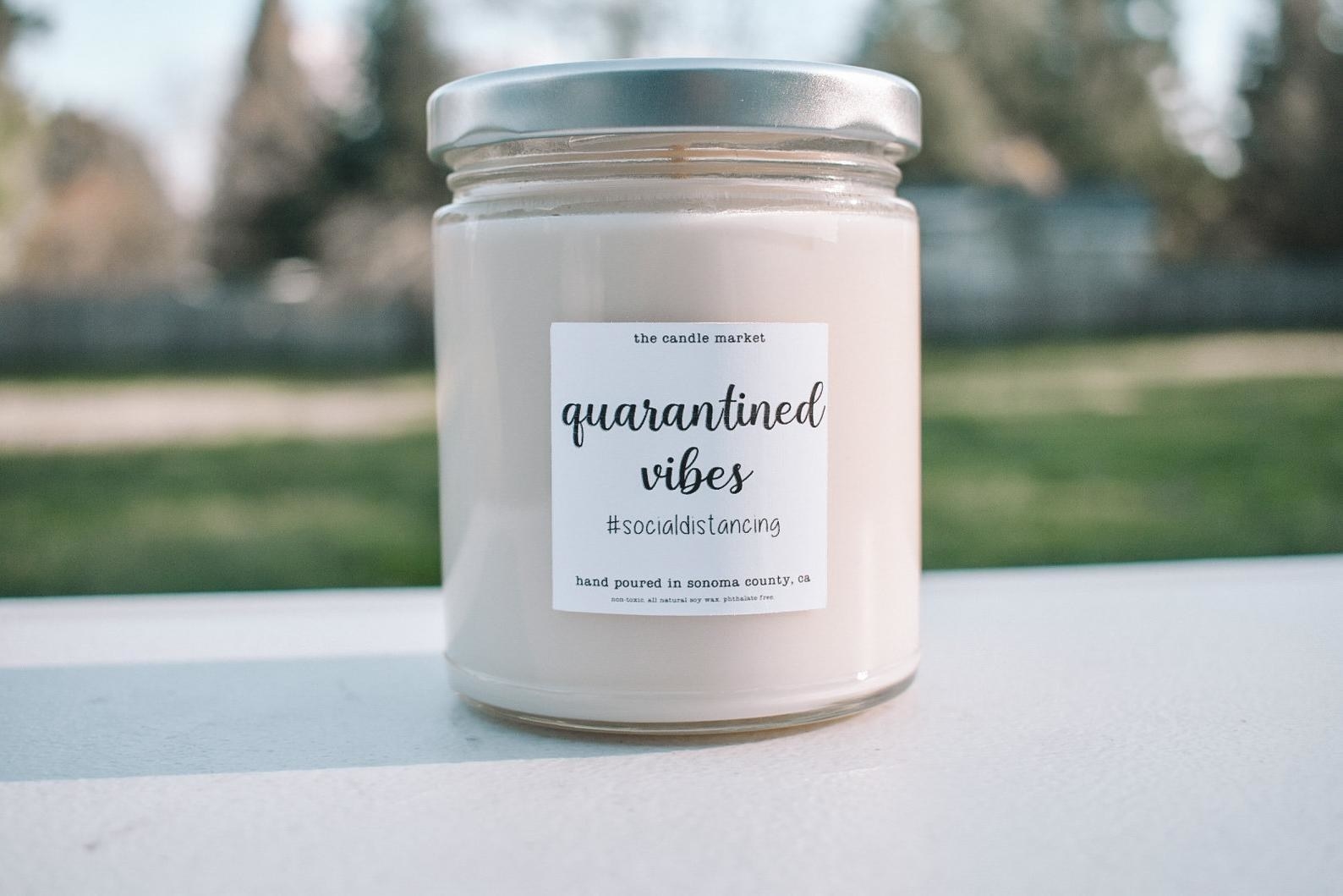 A white candle that says &quot;quarantined vibes&quot; 
