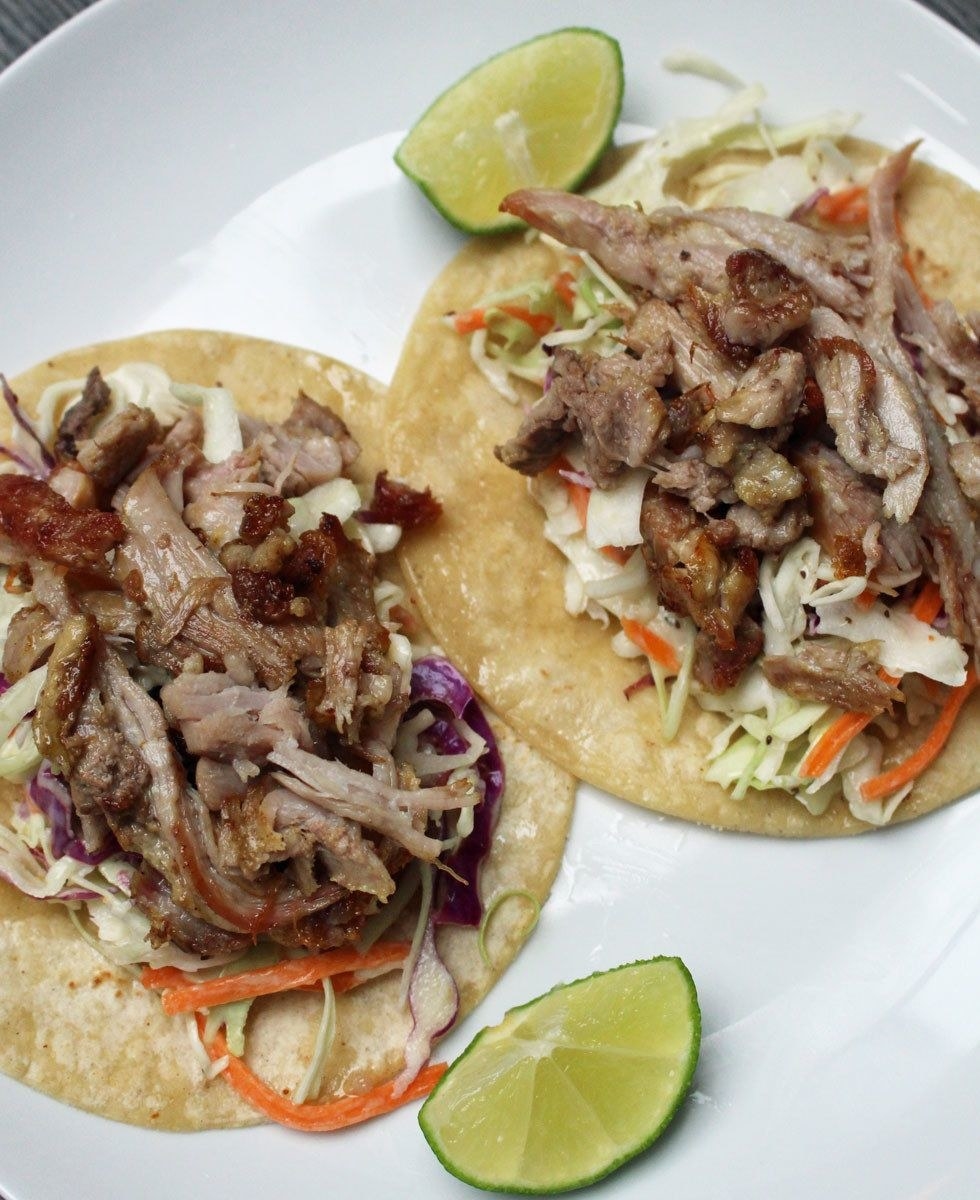 Two carnitas tacos with slaw on the bottom and a lime wedge on the side.