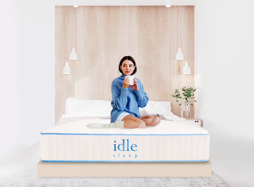 Model drinks coffee on white Idle Sleep Hybrid mattress on top of bed