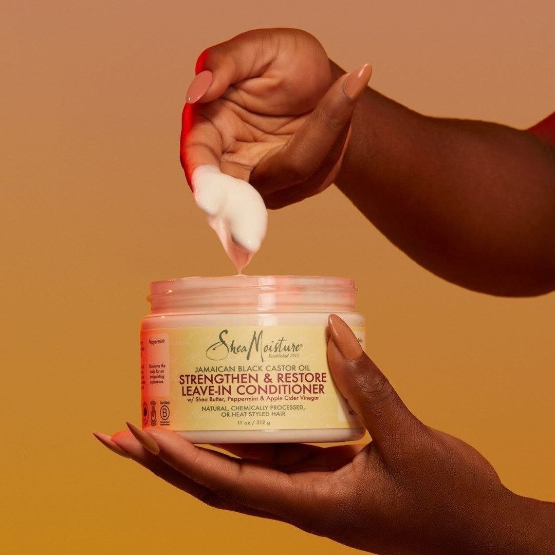 A person dips their fingers into the conditioner, showing off the rich creamy texture