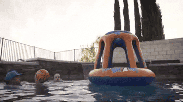 GIF of people in a pool dunking the ball into the inflatable hoop. One person is trying to block the shooter from getting the ball into the inflatable hoop.