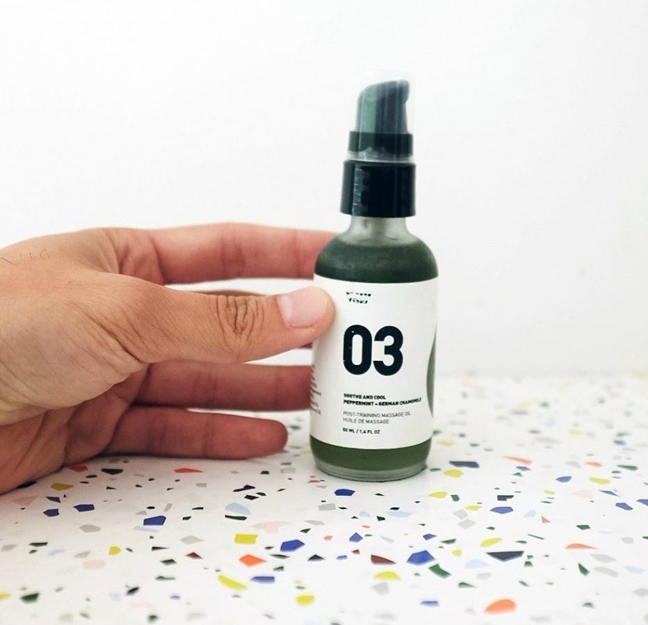 A person holds a bottle of the massage oil over a terrazzo countertop