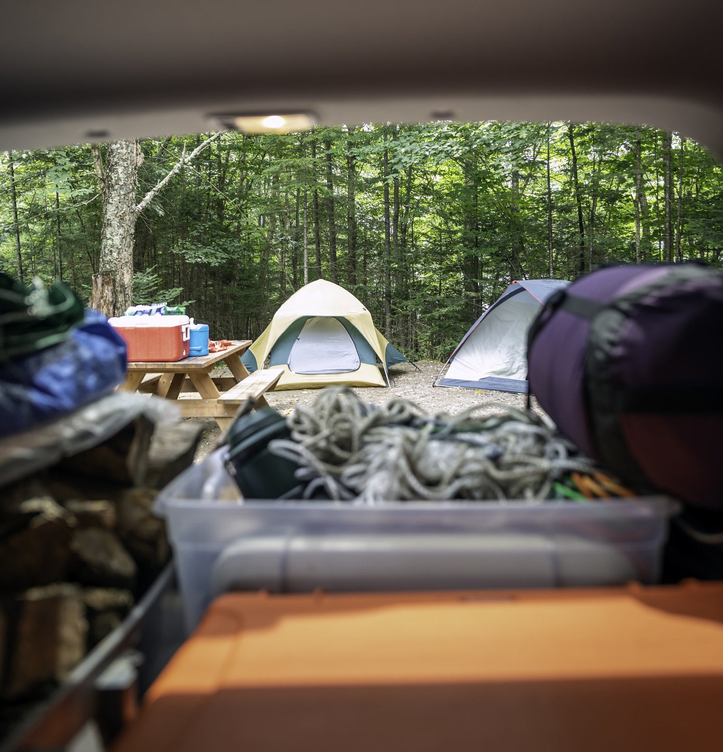 A car trunk full of camping gear with a tent in the background