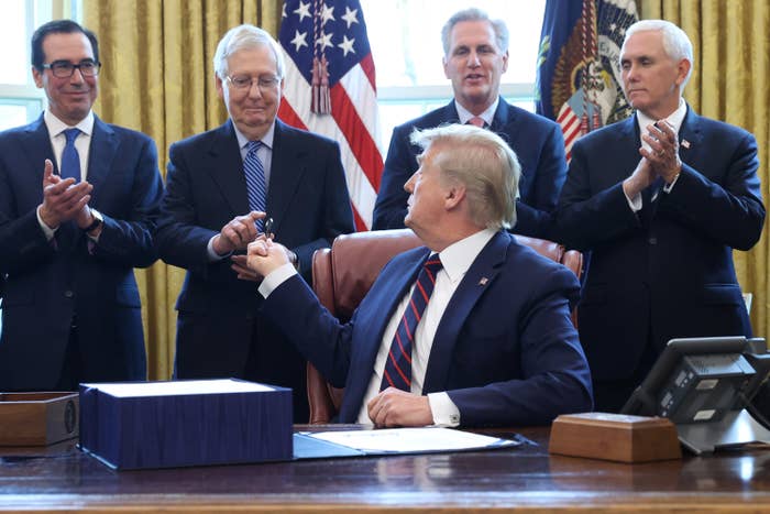 President Trump sits at the Resolute Desk in the Oval Office with Steven Mnuchin, Mitch McConnell, Kevin McCarthy, and Mike Pence applauding behind him
