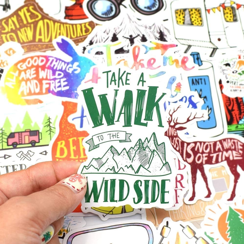 A person holding one mountain-themed sticker in front of a pile of stickers