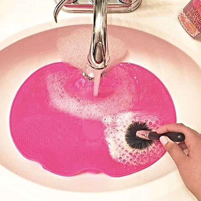A person washing their make-up brush using the cleaning brush at that’s been placed inside a sink.