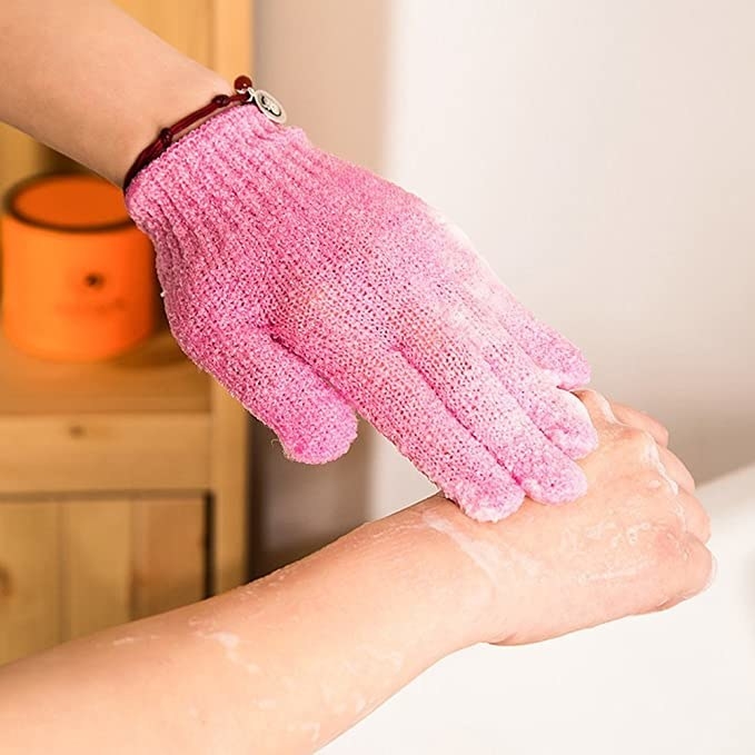 A person wearing a pink bath glove and exfoliating their arm. 
