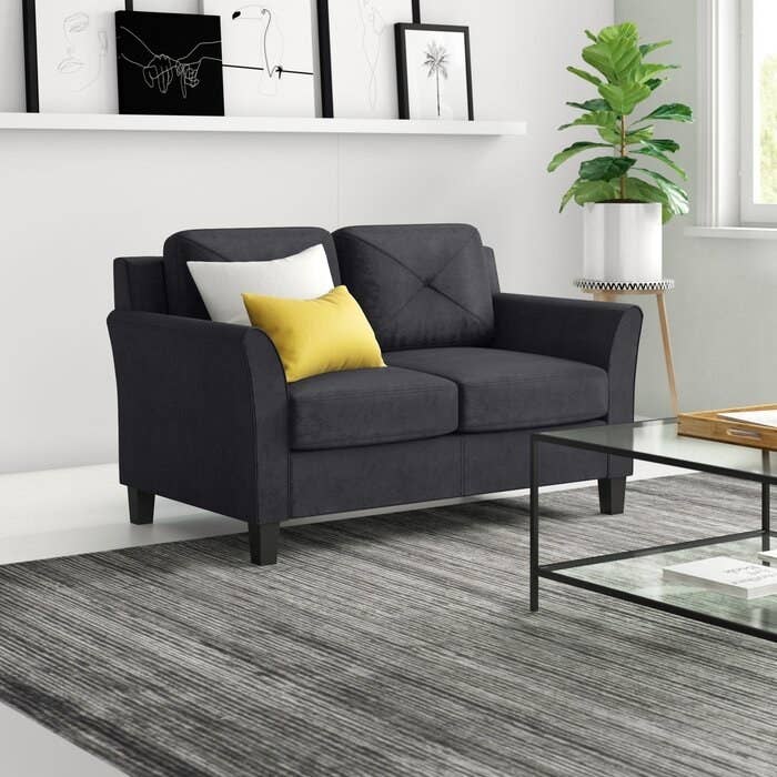Loveseat in black in black upholstery with wooden legs and a slightly tapered arms